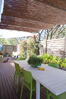 Terrasse en bois avec salle à manger informelle et moustiquaires lambrissées. Table avec rhipsalis en pot, écran mural vert avec des broméliacées assorties en arrière-plan