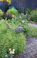 Jardin avec sculpture de poisson par Ulric Steiner nageant parmi une mer d'euphorbes naines 'Diamond Frost '. Derrière elle, des gerberas en fleurs