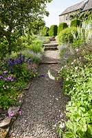 If 'butresses' sur le côté sud de la maison avec parterre de fleurs à côté du chemin planté d'Anemone rivularis, de digitales blanches, de géraniums rustiques et de campanules violettes.