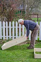 Construction de parterres surélevés dans un petit jardin. Homme plaçant un cadre de parterre surélevé.