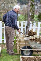 Construction de parterres surélevés dans un petit jardin. Homme remplissant un bac à compost de fumier de cheval. Il sera utilisé pour la culture de citrouilles.