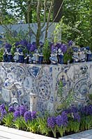 Figures hollandaises typiques en céramique Delfts Blue s'embrassant et placées sur le bord du bac à fleurs décoré rempli de Hyacinthus bleu. Jardin d'inspiration: Delfts Blue.