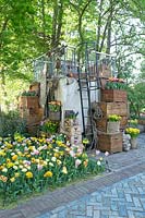 Petite maison en pot avec des boîtes en bois remplies de Narcisse et d'Hyancinthus. Escalier en fer menant à la terrasse sur le dessus. Jardin d'inspiration: l'âge d'or.