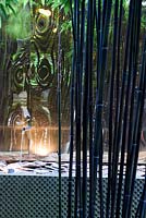 Tiges de bambou noir Phyllostachys nigra reflétées dans une tôle dorée brillante adossée à un élément d'eau avec un bec verseur.