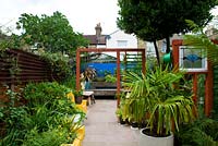 Vue sur jardin avec plantation de feuillage vert, aménagement paysager dur, séparateur de pièce en bois, mur peint en bleu et banc de dormeur en bois en pots