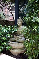 Statue de Bouddha en béton avec feuillage de bambou et camélia