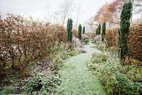 Dans la partie du jardin appelée Arcanum, un chemin d'herbe serpentant s'étend entre des parterres de plantes herbacées plantées de vivaces fleurissant dans une gamme de couleurs chaudes, y compris des astrantias, des achillées et des onagres, avec sept ifs irlandais fournissant de la hauteur.