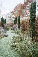 Dans la partie du jardin appelée Arcanum, un chemin d'herbe serpentant s'étend entre des parterres de plantes herbacées plantées de vivaces, y compris des astrantias, des achillées et des onagres, avec des ifs irlandais fournissant de la hauteur.