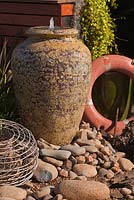 Section d'un jardin utilisant une collection d'éléments rustiques, un anneau de sauvetage, un pot Atlantis comme eau avec une succulente rampante, des Dischidia et un pot de homard