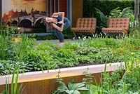 Un praticien de yoga dans Garden of Mindful Living avec deux chaises de Barcelone et des plantes vivaces, dont Epimedium et Hostas. The RHS Chelsea Flower Show 2016 - Designer: Paul Martin - Sponsor: Vestra Wealth LLP - OR