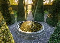 La lumière de l'aube brille à travers une porte d'entrée dans le jardin du puits avec ses ifs pyramidaux et ses tulipes, au Wollerton Old Hall Garden, Shropshire - photographié en avril