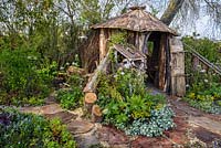 Cabane en bois et magasin de rondins avec Ajuga, Lamium, Euphorbia et Heuchera - Le jardin du bûcheron, RHS Malvern Spring Festival 2016. Conception: Mark Walker