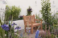 Un patio aux murs blancs, des parterres de fleurs surélevés avec des vivaces bleues, violettes et vert lime et un banc en bois naturel. Une bouffée d'air frais, RHS Tatton Flower Show 2011, Cheshire