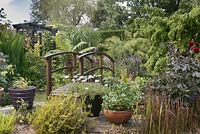 Vue sur le jardin avec petit pont en bois et arc de pergola - juillet, Cheshire