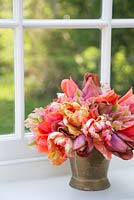 Bouquet de Tulipa 'Malaika', 'Temple of Beauty', 'Floriosa' et 'Apricot Parrot' dans un seau en laiton sur un rebord de fenêtre