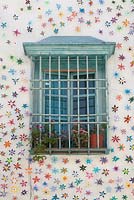 Fenêtre peinte en bleu pâle entourée de fleurs artificielles avec grille et pots de pélargoniums, Cordoue, Espagne