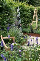Un jardin inspiré des arts et de l'artisanat avec un banc fait à la main, un obélisque et une sculpture en spirale. Une retraite d'été conçue par Laura Arison et Amanda Waring. RHS Hampton Court Flower Show 2016