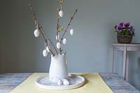 Oeufs de Pâques mouchetés suspendus à une branche avec fleur de printemps dans une cruche blanche