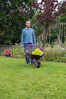 Homme portant des plantes dans une brouette dans le jardin, fille travaillant en arrière-plan