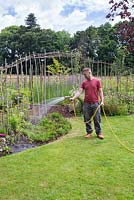 Un homme à l'aide d'un tuyau d'arrosage pour arroser les plantes dans un parterre de fleurs