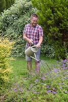 Un homme à l'aide d'un arrosoir pour arroser les plantes dans un parterre de fleurs