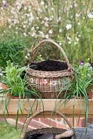 Étape par étape, plantez des paniers d'automne: un panier vintage rond est garni de tissu perméable, d'une couche de sable et rempli de compost prêt à être planté.