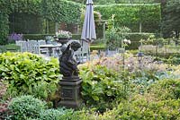 Vue depuis la terrasse: parterre de vivaces, statue d'ange enfant, jardin et urne décorative. Jardin Yvan et Gert En Belgique.