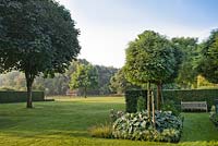 Vue sur le jardin. espace détente avec banc en bois, arbres matures, pelouse, haies et parterres de fleurs. Jardin d'Yvan et Gert en Belgique