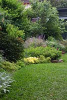 Vue d'un jardin montrant des parterres de jardin incurvés, une pelouse de buffle à feuilles souples et une variété de plantes herbacées à fleurs et de vivaces.