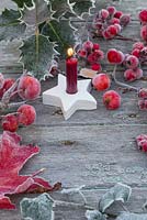 Bougie allumée rouge en étoile d'argile avec pommes sauvages givrées, baies d'aubépine et feuillage de houx