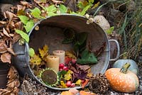 Arrangement dans un bassin en acier inoxydable contenant des bougies allumées, des malus, des citrouilles, des têtes de graines de tournesol et des feuilles d'automne