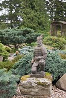 Une statue de guerrier en pierre dans un jardin de style japonais. conifères et roches. Juin, North Yorkshire.