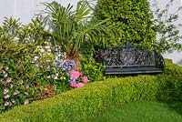 Un banc décoratif en fer forgé noir entouré de plantations tropicales colorées dans les grands jardins des États-Unis: le jardin de Charleston, RHS Hampton Court Flower Show 2016, conçu par Sadie May Stowell