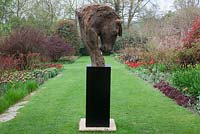 Sculpture 'Collected Head' de Kate Denton dans les parterres herbacés parsemés de tulipes aux couleurs chaudes