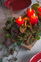 Une pièce maîtresse festive construite à partir de mousse, de pommes de pin, de bâtons de cannelle, de lierre, de tranches d'orange séchées et de bougies allumées
