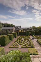 Une vue de la maison à travers le jardin de fantaisie avec son motif rose Tudor fabriqué à partir de la boîte - juin, Herterton House, Hartington, Northumberland, UK