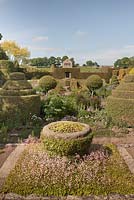 Une auge en pierre surélevée avec du lierre et de la fierté de Londres et une vue sur le jardin de fleurs de la maison avec des formes topiaires à l'aide de la boîte et l'if - juin, Herterton House, Hartington, Northumberland, UK