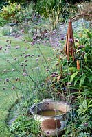 Little Ash Garden, Fenny Bridge, Devon. Seau en métal en automne parterre de fleurs avec Verveine bonariense et sculptures en métal