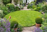 Une pelouse circulaire est entourée de parterres herbacés de style chalet de menthe des chats, géranium rustique, marguerite, scabieuse, hortensia, lavande, roses et digitales.
