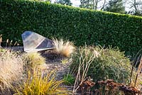 Siège en ardoise simple dans le jardin de gravier entouré d'herbes à feuilles caduques et de Libertia 'Goldfinger '. Windy Ridge, Little Wenlock, Shropshire, Royaume-Uni