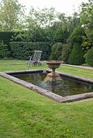 Étang et fontaine en pierre vieillie avec banc en bois. Jardin: Rustling End Cottage, Hertfordshire. Propriétaires: M. et Mme Wise