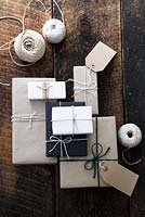 Beaucoup de cadeaux enveloppés de papier brun et blanc et attachés avec de la ficelle, avec des étiquettes-cadeaux et de la ficelle.