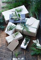 Beaucoup de cadeaux enveloppés de papier brun et blanc et attachés avec de la ficelle, avec des étiquettes-cadeaux et de la ficelle. Décoré de sapin, d'if et de feuillage argenté