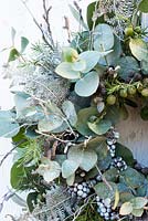 Couronne de Noël blanche et argentée avec des baies de genévrier euclayptus et des feuilles de fougère blanche pulvérisées, des baies de lierre et des brindilles