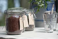 Bocaux en verre étiquetés remplis de différents thés et verres à thé sur une table.