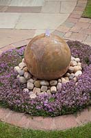 Sphère de pierre arc-en-ciel caractéristique de l'eau entourée de galets et de plantes de thymus - juin, Summerfield Place, Cheshire