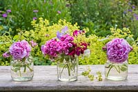 Arrangement floral d'été dans des bocaux en verre avec des roses, Alchemilla mollis, Dianthus barbartus, pois de senteur et fragaria barbartus