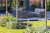 Un patio, avec des sièges et une rigole, dans un jardin de campagne moderne du Cheshire, conçu par Louise Harrison-Holland. La plantation comprend des couvertures en boîte, Stachys, Ophiopogon planiscapus 'Nigrescens', des anémones japonaises et un Pelargonium en pot