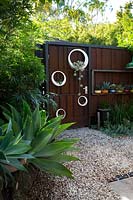 Une porte en acier corten rouillé avec un groupe de pots en métal circulaires peints à la main en blanc et plantés de plantes succulentes. Les pots comprennent un Agave attenuata, une plante Century et du bambou.