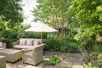 Meubles en osier sur terrasse en été avec Rosa, Stipa gigantea et pots décoratifs mixtes